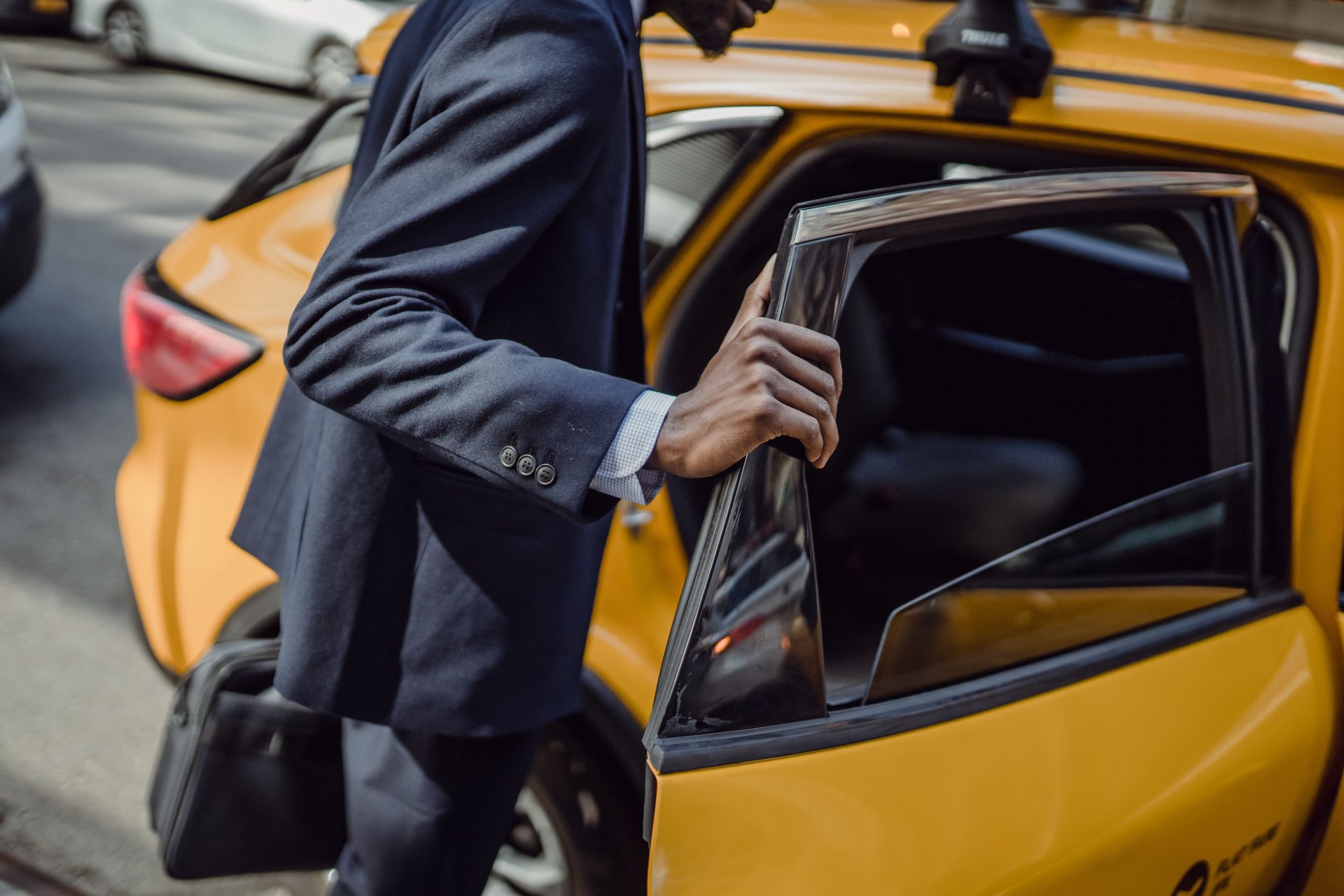Ein Geschäftsmann im Anzug öffnet tagsüber auf einer Stadtstraße die Tür eines gelben Taxis.