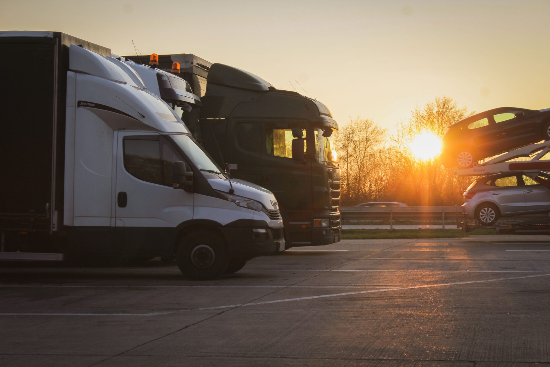 Eine Reihe von Lastwagen und Autotransportern steht bei Sonnenuntergang auf einem offenen Parkplatz und hebt die Stimmung der „goldenen Stunde“ hervor.