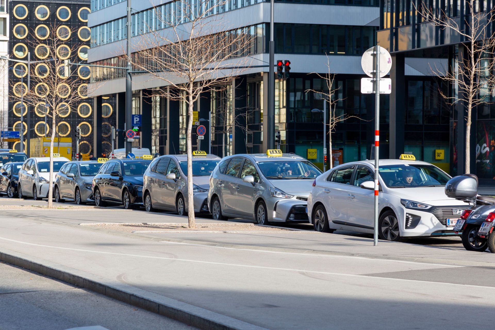 Eine Reihe von Taxis auf einer städtischen Straße mit modernen Gebäuden im Hintergrund.