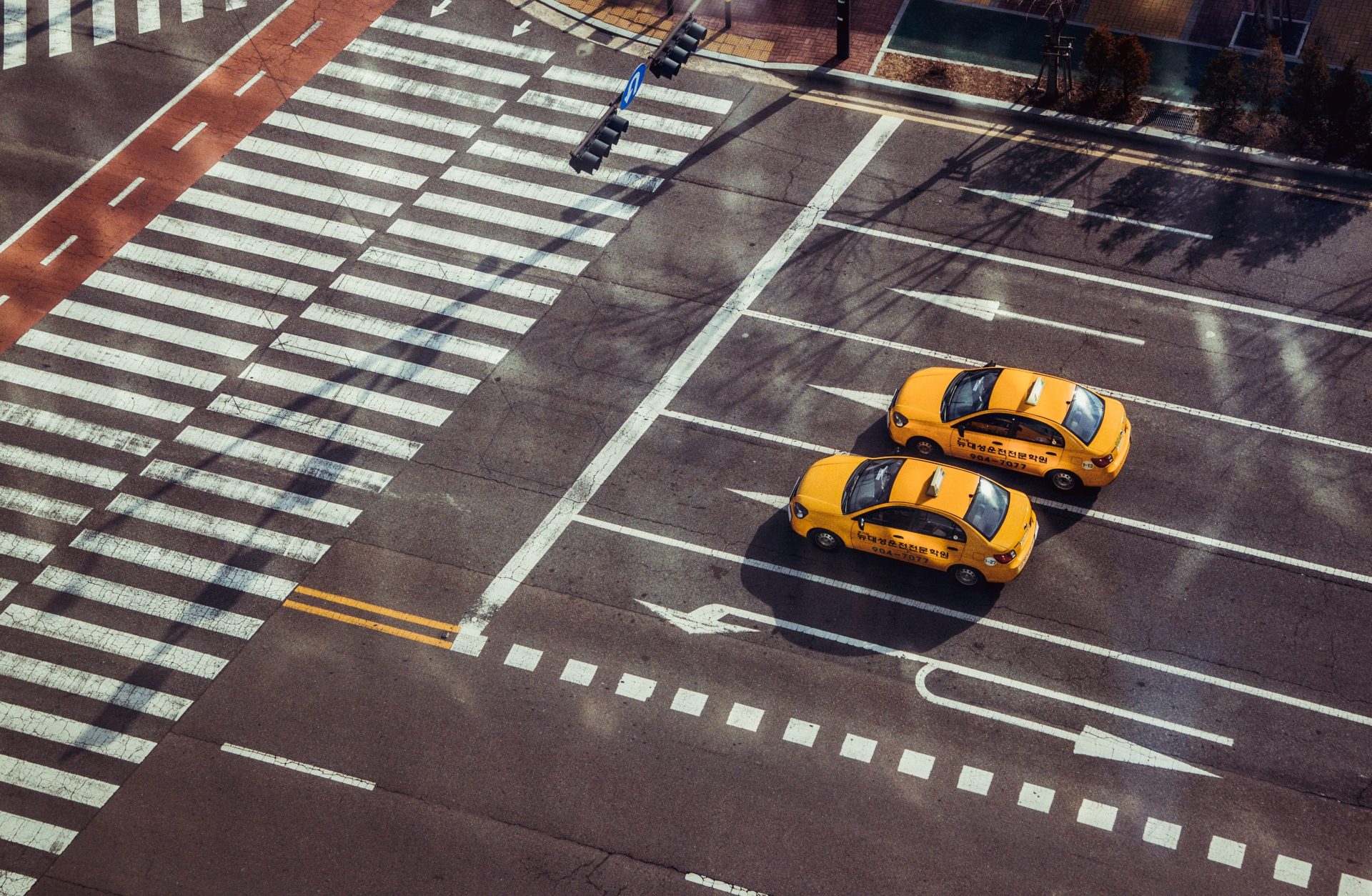 Zwei gelbe Taxis fahren über eine städtische Kreuzung mit markierten Fußgängerüberwegen.